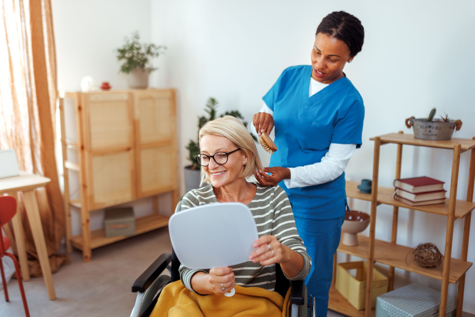 Female nurse helping mature woman in wheelchair to do her hair during home visit